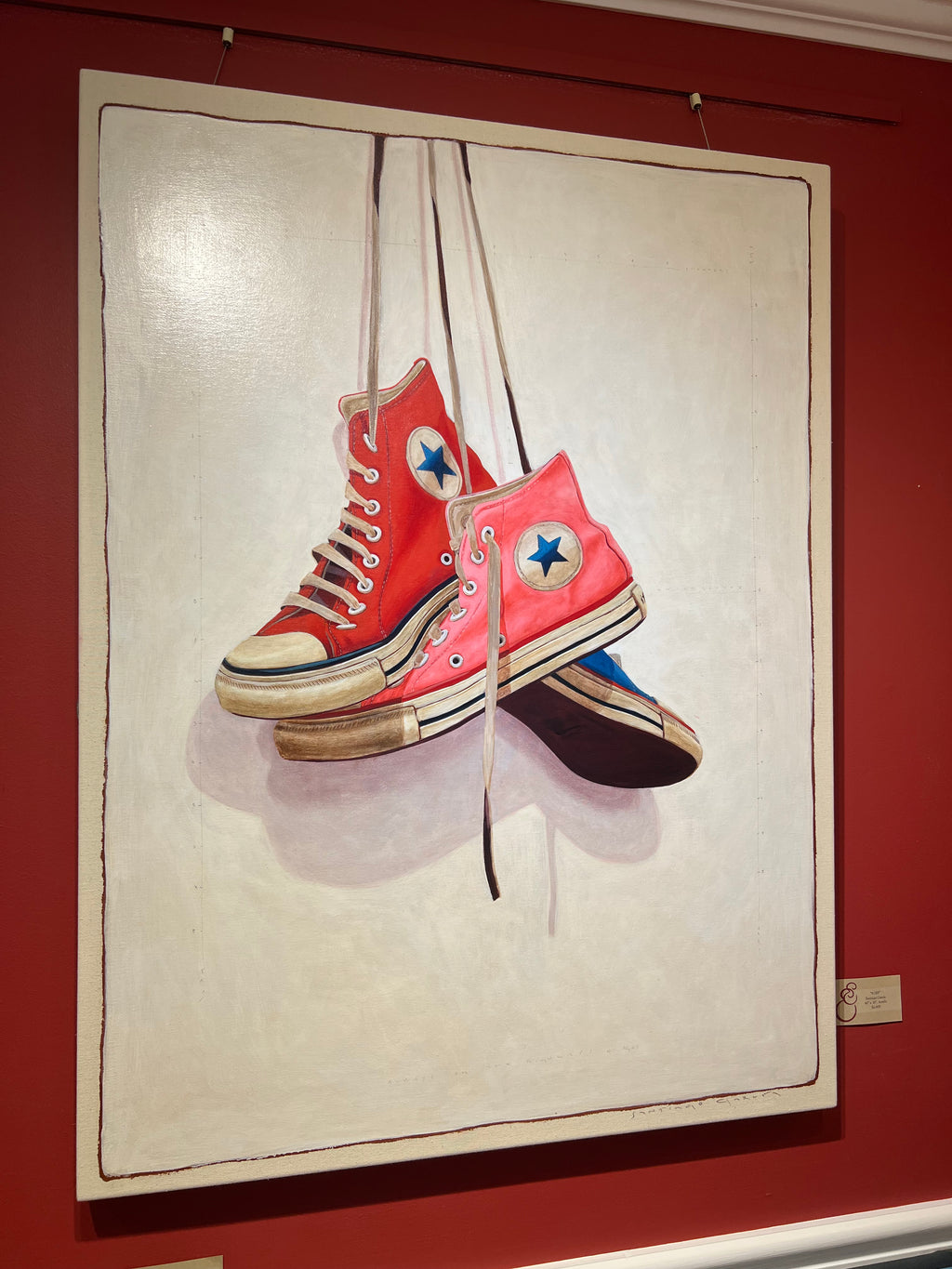 photorealistic oil painting of red, pink, and blue high top converse sneakers hanging by laces