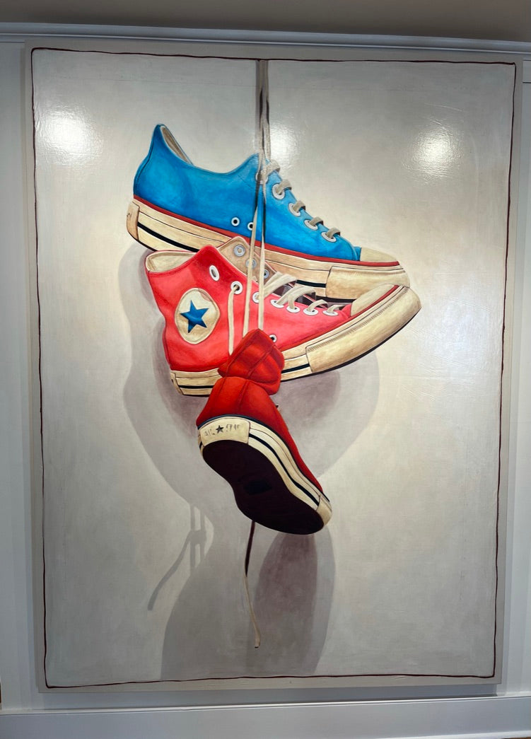 Still life oil painting by Santiago Garcia of a red, blue, and pink converse sneaker hanging by shoe laces on a white shadowed canvas