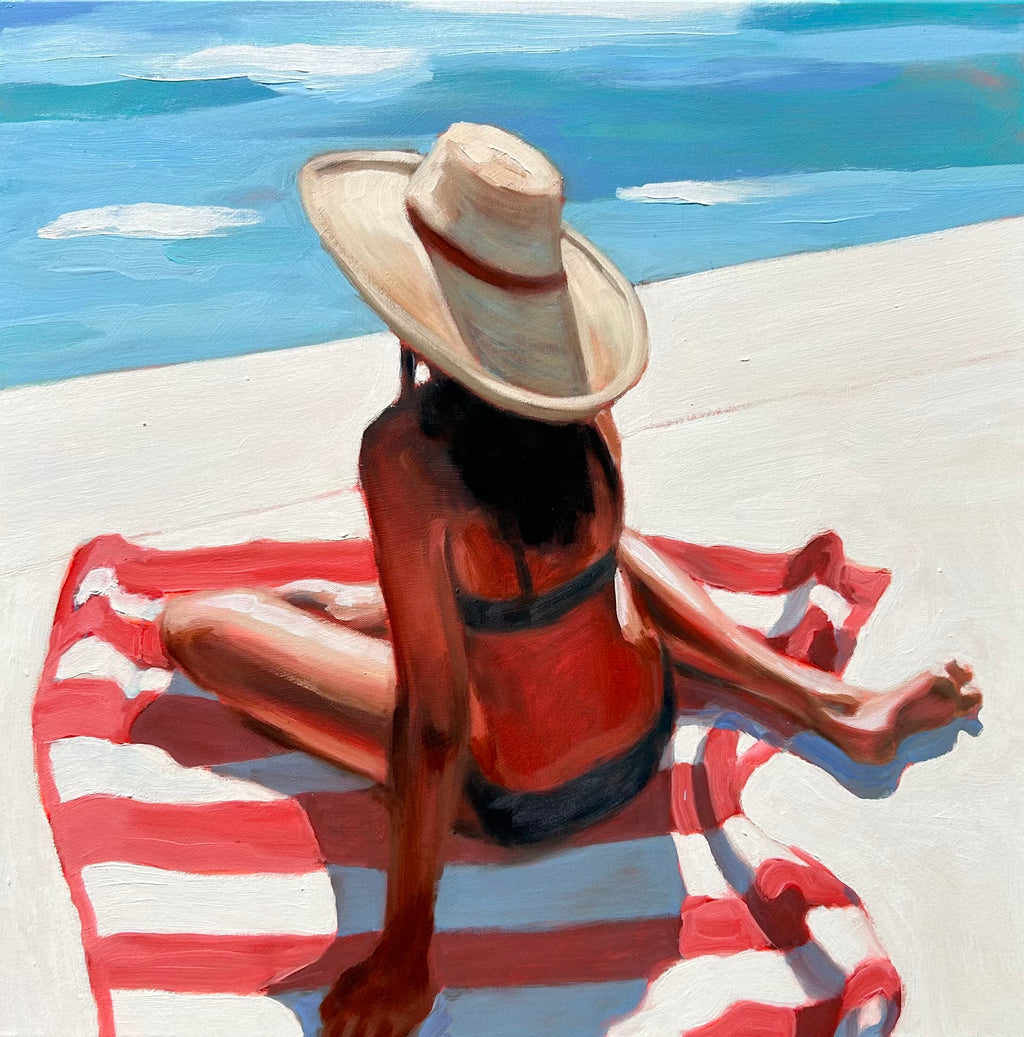 woman sits poolside on a red and white striped towel. She wears a hat to shade her from the sun.