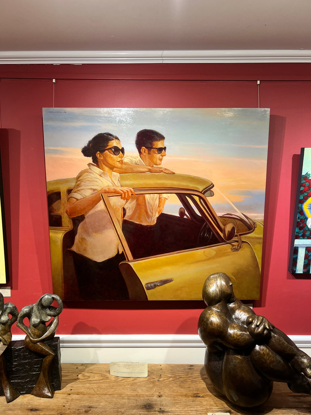 Oil painting by Joseph Lorusso of a man and a woman standing on either side of a yellow car both wearing sunglasses against a pastel sunset sky.