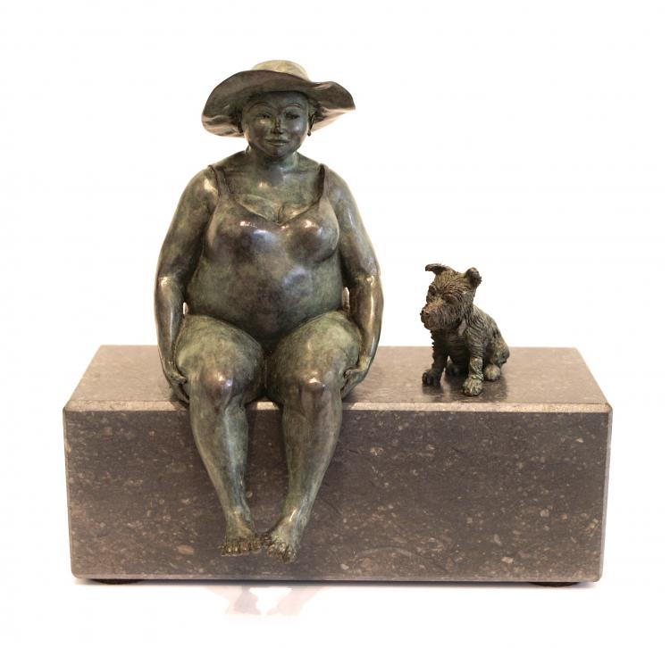 Bronze sculpture by Veronique Clamot of a plus sized model sat on a bench next to a small dog wearing a sunhat