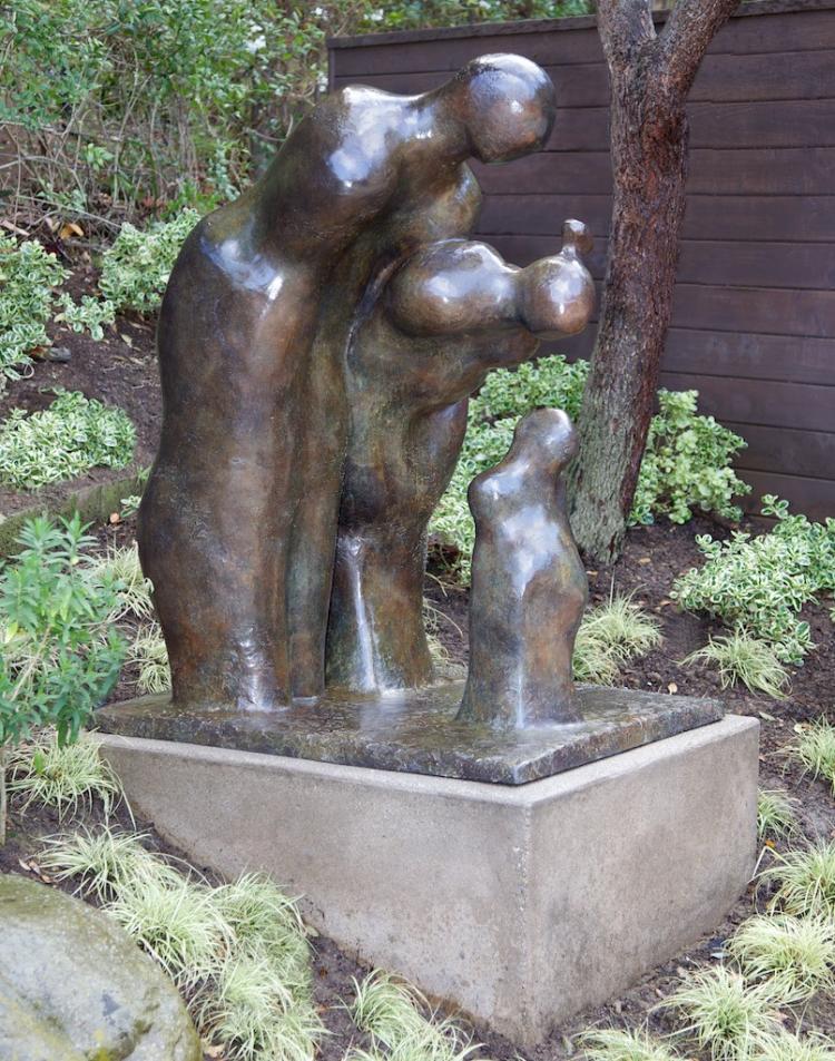 Contemporary life size bronze figurative sculpture of parents bending over a child